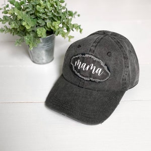 May include: A black distressed baseball cap with a white oval patch that says "mama" on it.