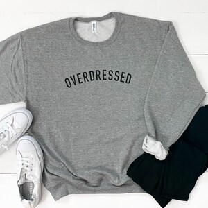 May include: Gray sweatshirt with the text "OVERDRESSED" printed in black on the front.