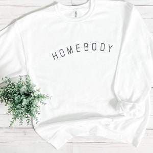 Puede incluir: Sudadera blanca con el texto "HOMEBODY" impreso en negro en la parte delantera.