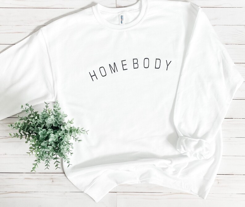 Puede incluir: Sudadera blanca con el texto "HOMEBODY" impreso en negro en la parte delantera.