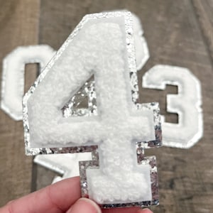 May include: White felt number four with a silver glitter outline. The number is a patch or applique.