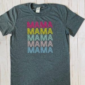 May include: A dark grey t-shirt with the word "MAMA" repeated five times in a rainbow color scheme. Each word is outlined in yellow.