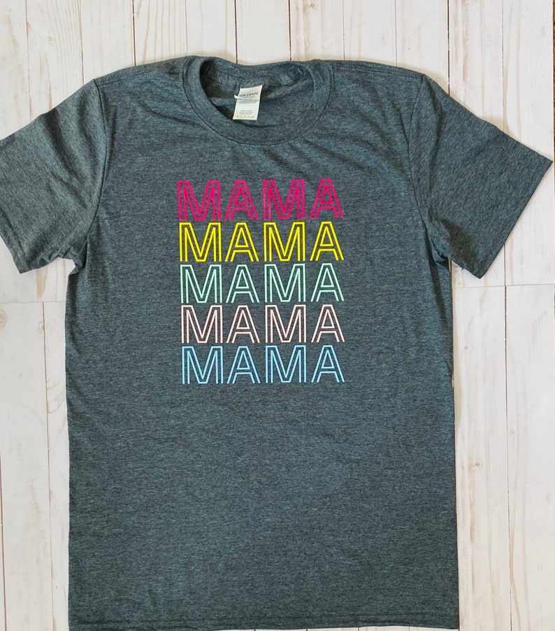 May include: A dark grey t-shirt with the word "MAMA" repeated five times in a rainbow color scheme. Each word is outlined in yellow.