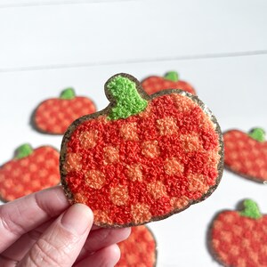 May include: A set of six orange and red fuzzy pumpkin patches with green stems. The pumpkins are arranged in a circle on a white surface.