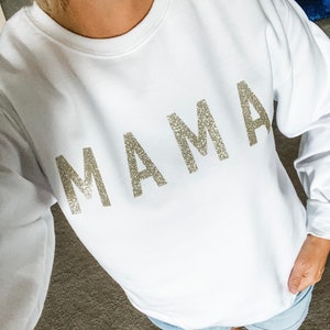 May include: White sweatshirt with the word "MAMA" in sparkly silver letters.