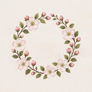 Op de afbeelding: Een cirkelvormig bloemenborduurontwerp met een krans van roze bloesems, knoppen en groene bladeren op een crèmekleurige stoffen achtergrond. De bloemen hebben gele centra en zijn symmetrisch gerangschikt.
