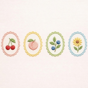 Puede incluir: Cuatro parches ovalados bordados con bordes festoneados. Cada parche presenta un diseño diferente: cerezas, un melocotón, arándanos y un girasol. Los parches son de colores pastel, sobre un fondo blanco.