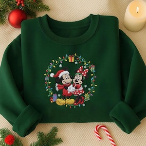 May include: A dark green sweatshirt featuring an embroidered design of Mickey and Minnie Mouse in Christmas attire, surrounded by a wreath of lights, gifts, and snowflakes. The sweatshirt has a crew neck and long sleeves.