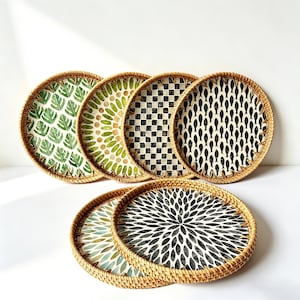 May include: A collection of round rattan trays with various decorative patterns. Designs include green leaves, olive-colored circles, black and white checkered, and fish scale patterns. The trays are suitable for serving or display.