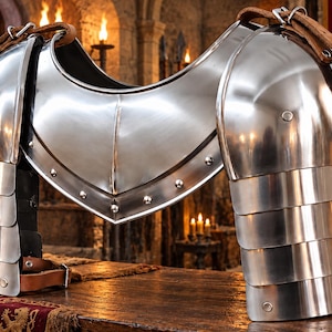 May include: A polished steel pauldrons and gorget set featuring articulated metal plates for the shoulders and upper chest. The armor includes brown leather straps with metal buckles for secure fastening and silver rivets along the edges.