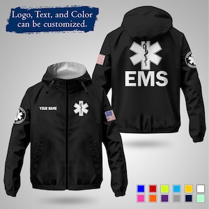 Può includere: Giacca con cappuccio nera con testo bianco "EMS" e un emblema bianco a forma di Stella della Vita. Presenta una toppa con la bandiera americana sulla manica e la scritta "YOUR NAME" sopra un emblema più piccolo. È visibile anche il testo "Logo, Text, and Color can be customized".