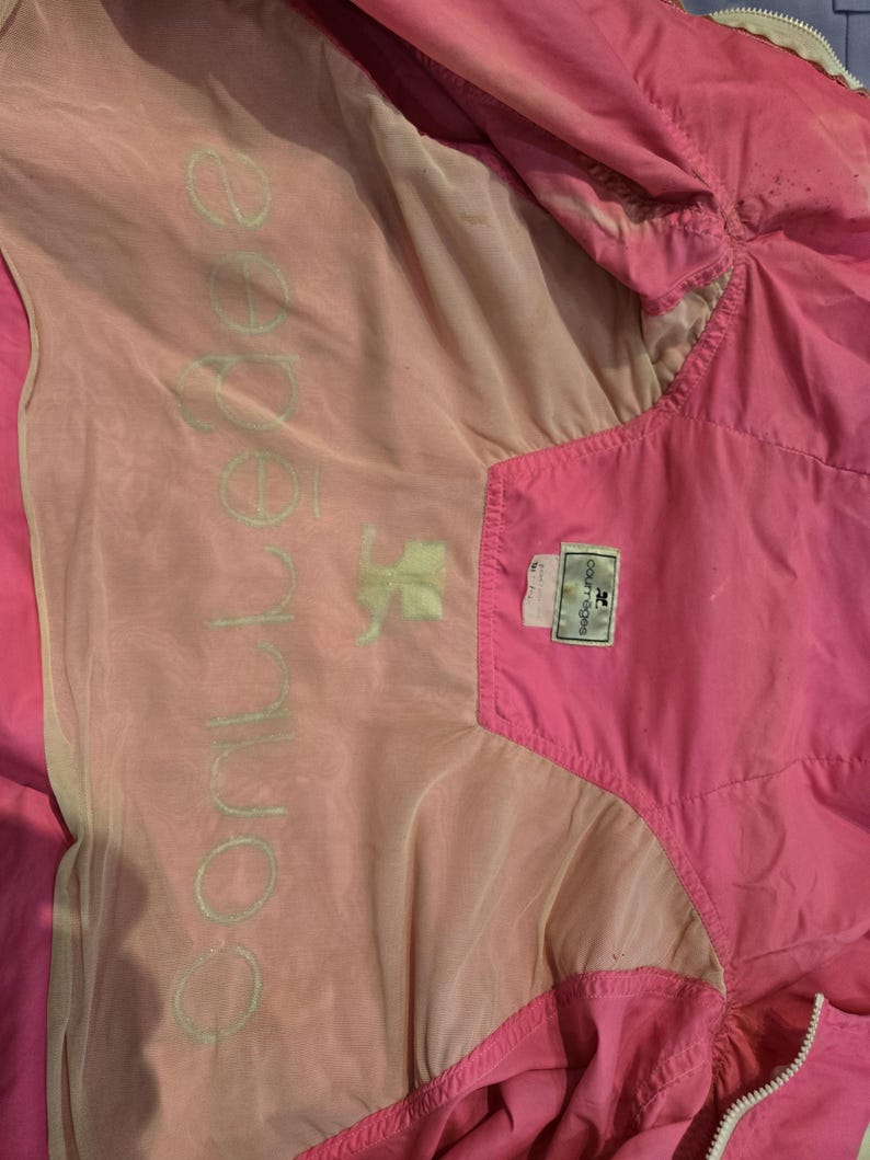 May include: Bright pink windbreaker jacket with a light pink and beige lining. The jacket has a zipper closure and a tag with the brand name. The interior lining features the word "conner" in a light green color.