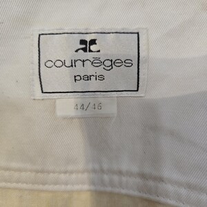 May include: Close-up of a white fabric tag with the text "courr&egrave;ges paris" in black, and the size "44/46" in black. The tag is rectangular with a black border and the Courr&egrave;ges logo. The fabric is a light cream color.