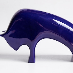 May include: A blue ceramic sculpture of a bull with a sleek, modern design. The bull is depicted in a dynamic pose, with its head lowered and its horns pointed forward.