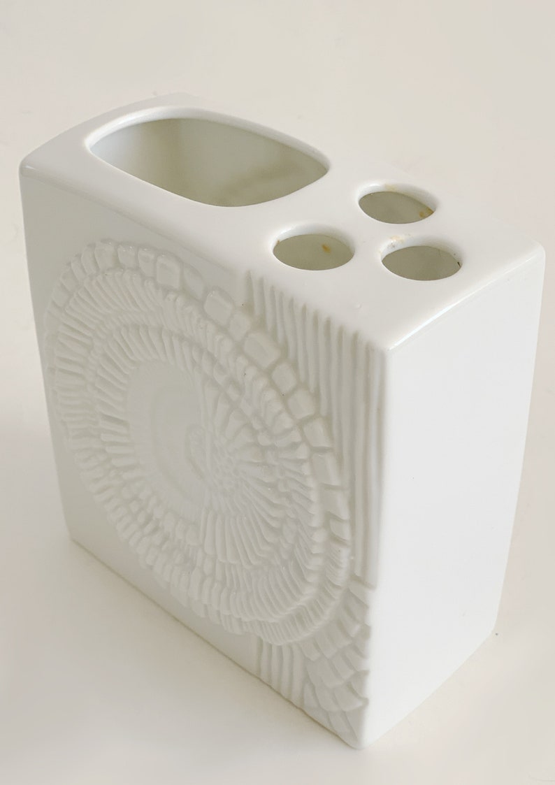 Puede incluir: Un portacepillos de cer&aacute;mica blanca de forma rectangular. Cuenta con una gran abertura ovalada y tres peque&ntilde;os orificios circulares. El frente tiene un dise&ntilde;o circular texturizado en relieve. Un accesorio de ba&ntilde;o.