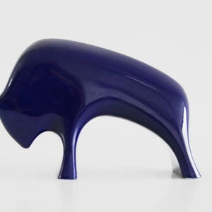 May include: A blue ceramic sculpture of a stylized bull. The bull is standing on its hind legs with its head lowered. The sculpture is made of a smooth, glossy ceramic.