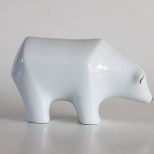 May include: A white ceramic polar bear figurine with gold accents. The bear is standing on all fours and has a simple, stylized design.