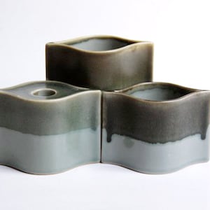 Puede incluir: Tres portavelas de cerámica con forma de lágrima ondulada. Los portavelas están esmaltados en un esquema de colores azul claro y verde oscuro.