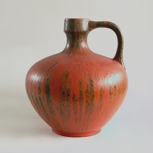 Puede incluir: Un jarrón de cerámica rojo y verde con una base ancha y un asa. El jarrón tiene una superficie texturizada y un esmalte moteado.