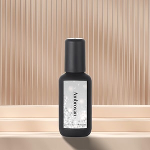 May include: A black perfume bottle with a rectangular label. The label features the word "Ambroxan" in white, with a silver glitter design. The bottle has a black cap and the text "Scent 02" is at the bottom of the label.