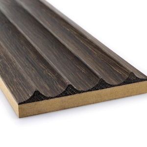 Könnte beinhalten: Nahaufnahme einer dunkelbraunen Holzplatte mit gerilltem Design. Die Platte hat eine strukturierte Oberfläche und eine hellbraune Basis. Die Rillen verlaufen parallel und erzeugen ein sich wiederholendes Muster. Die Holzmaserung ist sichtbar.