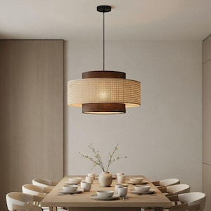 May include: A modern dining room featuring a large wooden table set for a meal. Above the table hangs a two-tiered pendant light with a woven shade and dark wood accents. The room has light-colored walls and matching chairs.