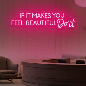 May include: A neon sign with the text "IF IT MAKES YOU FEEL BEAUTIFUL Do it" in bright pink. The sign is mounted on a pink tiled wall. The scene includes a reception desk and hanging lights.