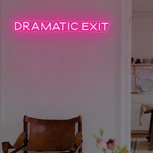 May include: A bright pink neon sign that reads "DRAMATIC EXIT" is mounted on a white wall. Below the sign is a brown leather chair. The background shows a glimpse of a kitchen with a table and chairs.
