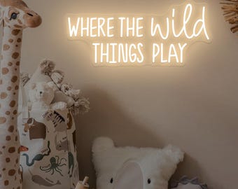 Op de afbeelding: Een kinderkamerscène met een girafknuffel, een canvas tas met dierenillustraties en een wit neonbord met de tekst "WHERE THE WILD THINGS PLAY". Andere knuffels zijn een beer en een dinosaurus.