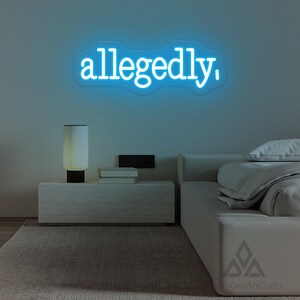 以下が含まれることがあります： 雲の形をしたネオンサインには、明るい青色で「allegedly」という言葉が表示されています。このサインは、ランプ、本、ベッドのあるナイトテーブルの上にある明るい色の壁に取り付けられています。