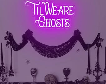 May include: A neon sign in a purple hue displays the text "Til We Are Ghosts." The sign is mounted above a Halloween-themed display. The display includes black lace, decorative goblets, skulls, and ornate candle holders, creating a spooky ambiance.