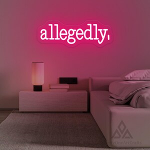 以下が含まれることがあります： 寝室のネオンサインには、白い文字で「allegedly」という言葉が表示されています。このサインは、ピンク色の壁に取り付けられており、ランプ、本、ピンク色の掛け布団が付いたベッドのあるナイトスタンドの上にあります。