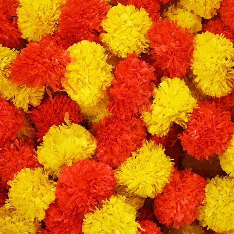 May include: Close-up of a vibrant collection of artificial marigold flowers in shades of yellow and orange. The flowers are densely packed, creating a textured and colorful display. Ideal for festive decorations.
