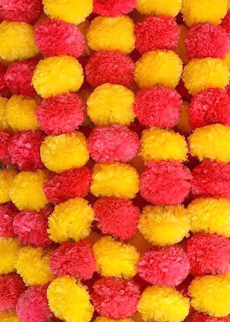 May include: Close-up of a vibrant garland composed of alternating rows of yellow and red pom-pom-like flowers. The flowers are densely packed, creating a textured and colorful display. The bright colors suggest a festive or decorative theme.