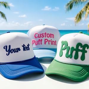 Könnte beinhalten: Drei Trucker-Caps mit weißen Frontplatten und farbigen Schirmen. Eine Kappe ist blau mit "Your text" in Marineblau, eine andere hellblau mit "Custom Puff Print" in Rosa und die dritte grün mit "Puff" in Grün.