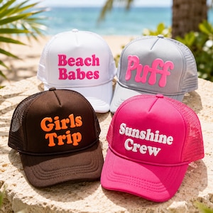 May include: Four foam and mesh trucker hats with adjustable snapback closures. One white hat with pink text reading Beach Babes, one gray hat with pink text reading Puff, one brown hat with orange text reading Girls Trip, and one hot pink hat with white text reading Sunshine Crew.