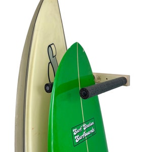 May include: Two surfboards mounted on a wall rack. The surfboard on the left is white with a black stripe. The surfboard on the right is green with a white stripe and a "Surf Station Surfboards" logo.