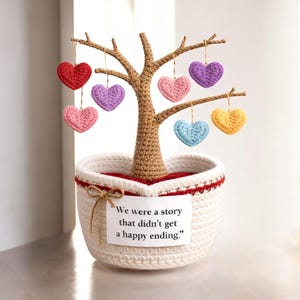 May include: A handcrafted crochet tree with a brown trunk and branches, planted in a white basket. The tree is adorned with colorful crochet hearts in red, pink, purple, blue, and yellow. A tag reads, "We were a story that didn't get a happy ending."