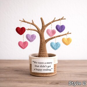May include: A crocheted tree with brown trunk and branches, adorned with colorful heart-shaped ornaments. The tree is potted in a beige basket. A tag reads, "We were a story that didn't get a happy ending." Style 2 is displayed at the bottom right.