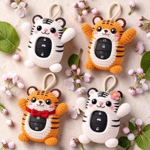 May include: Four crocheted tiger-shaped car key covers with black plastic key fobs visible in the center. Two covers are white with black stripes, and two are orange with black stripes. One orange cover has a red bow tie, and one white cover has a small pink flower.