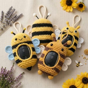 May include: Three crocheted bee-shaped key fob covers with black and yellow stripes, antennae, and small wings. Each cover features a central cutout to hold a black car key fob. The designs include light blue, white, and cream-coloured wings.