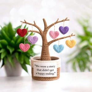 May include: A handcrafted crochet tree with a brown trunk and branches, adorned with colorful heart-shaped ornaments. The tree is planted in a woven pot with a label that reads, "We were a story that didn't get a happy ending."