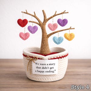 May include: A crocheted tree with a brown trunk and branches, planted in a white basket with a red trim. The tree holds several hanging, colorful crocheted hearts. A tag on the basket reads, "We were a story that didn't get a happy ending."
