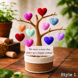 May include: A decorative tree with a brown trunk and branches, adorned with colorful, crocheted hearts. The base is a woven basket with a white band. A sign reads, "We were a story that didn't get a happy ending."