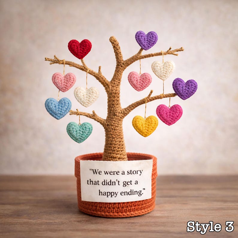 May include: A crocheted tree with a brown trunk and branches, adorned with colorful hanging hearts. The tree sits in a terracotta-colored pot with a label that reads, "We were a story that didn't get a happy ending."
