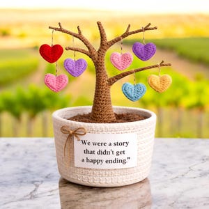May include: A handcrafted crochet tree with a brown trunk and branches, planted in a white woven pot. The tree is adorned with hanging crochet hearts in red, pink, purple, blue, and yellow. A tag reads, "We were a story that didn't get a happy ending."