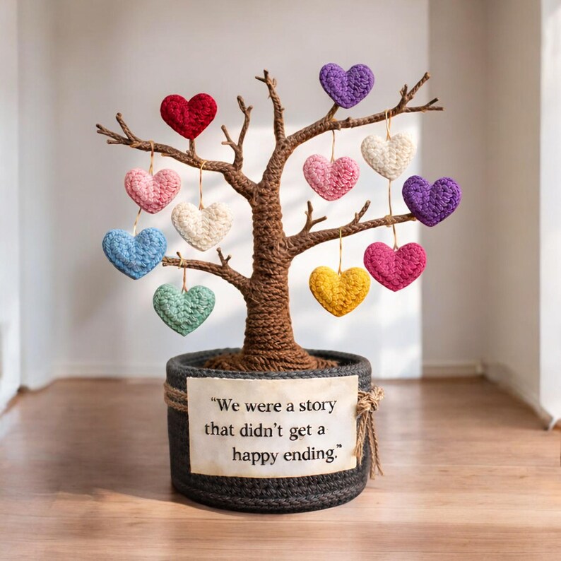 May include: A handcrafted tree sculpture with a woven trunk and branches, adorned with colorful crocheted hearts. The tree sits in a dark gray pot with a decorative rope trim. A tag reads, "We were a story that didn't get a happy ending."