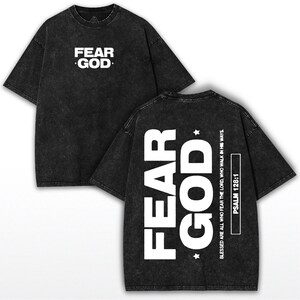 May include: Two-sided, dark gray t-shirts with white text. The front of the shirt reads "FEAR GOD." The back of the shirt features the words "FEAR GOD" vertically, with "BLESSED ARE ALL WHO FEAR THE LORD, WHO WALK IN HIS WAYS" and "PSALM 128:1."