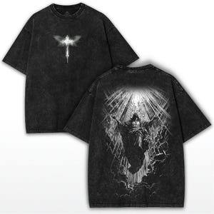 May include: Black acid wash t-shirt featuring a graphic of a cross with wings on the front and a detailed illustration of a figure with outstretched arms on the back. The shirt has a vintage, worn look.