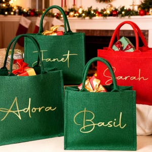 Könnte beinhalten: Vier Tragetaschen, drei grüne und eine rote, gefüllt mit Geschenken. Die grünen Taschen tragen die Namen "Adora", "Janet" und "Basil" in goldfarbenen Buchstaben. Die rote Tasche trägt den Namen "Sarah" in goldfarbenen Buchstaben. Die Taschen haben grüne Griffe.
